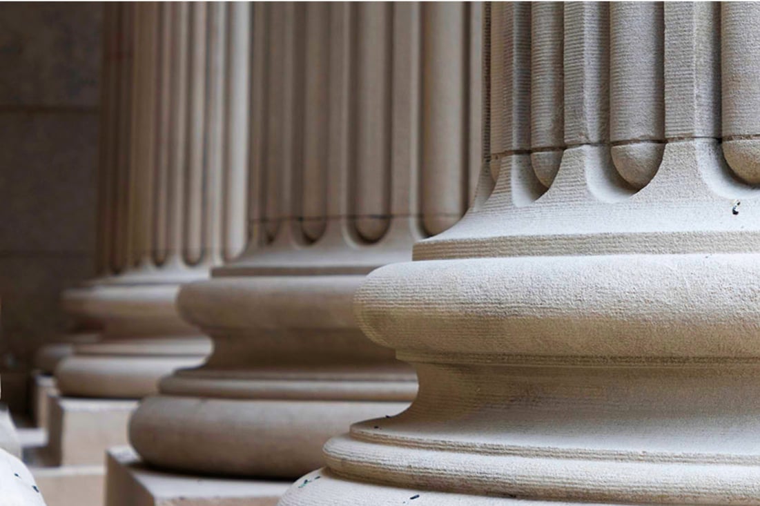 Row of large classical stone columns viewed from the base, showing smooth rounded pedestals and vertical fluting in soft light.